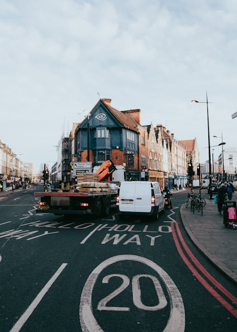 A dark red flatbed van parked on a city street in Putney, with its cargo area filled with various household items, including large plastic bags, wrapped furniture, and cardboard boxes. The items are a
